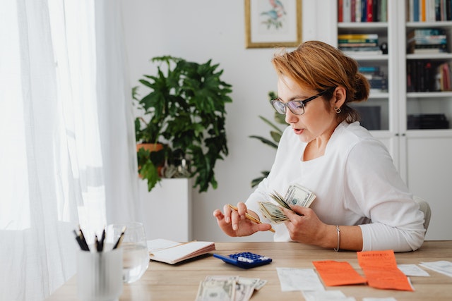 person holding a stack of cash while adding it up on a calculator