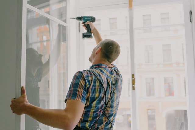 someone-in-a-plaid-shirt-using-a-drill-to-fix-a-window