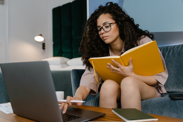 person sitting on a couch working on a laptop and writing in a yellow notebook