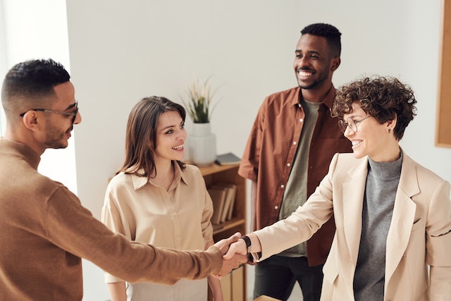 four people standing together, two of them shaking hands