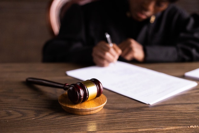 Wooden gavel in the foreground with a lawyer signing a document in the background