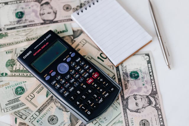 A calculator, a notepad, and several American banknotes.