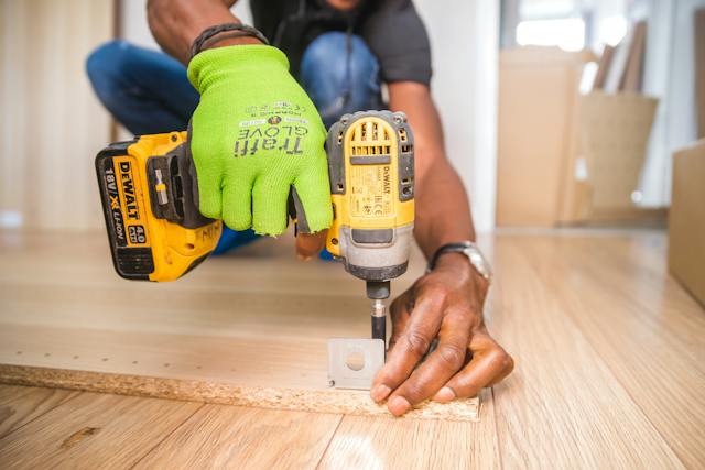 A person drilling into a board on the floor.