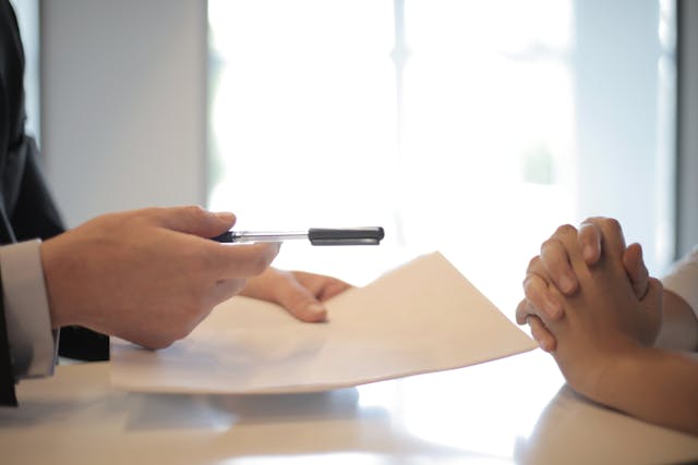 One person passing a paper and pen to another across a table.